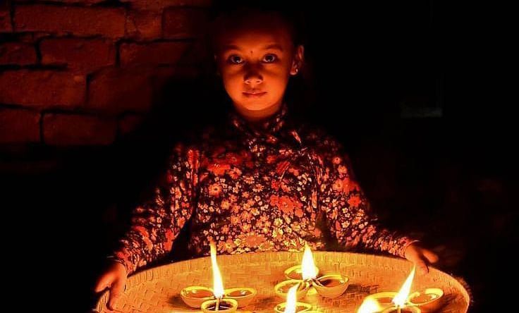 A young girl holding a diyas placed on a plate