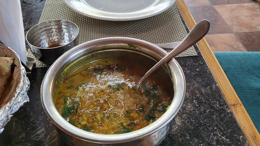 A dining table set with a bowl of curry, cutlery, and a plate in a restaurant setting at Dagshai Manor Kasauli - Inde Hotels.