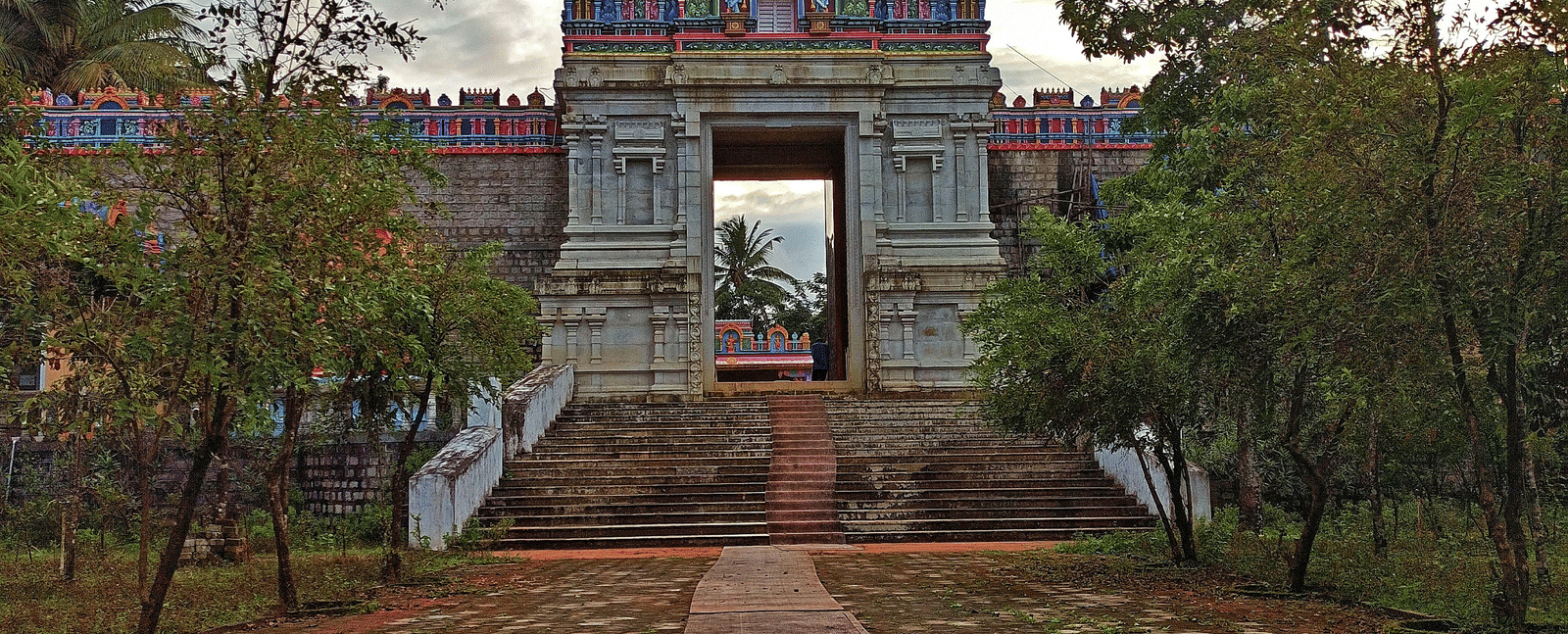 A vibrant temple with a colourful gopuram, framed by lush trees under a bright sky.