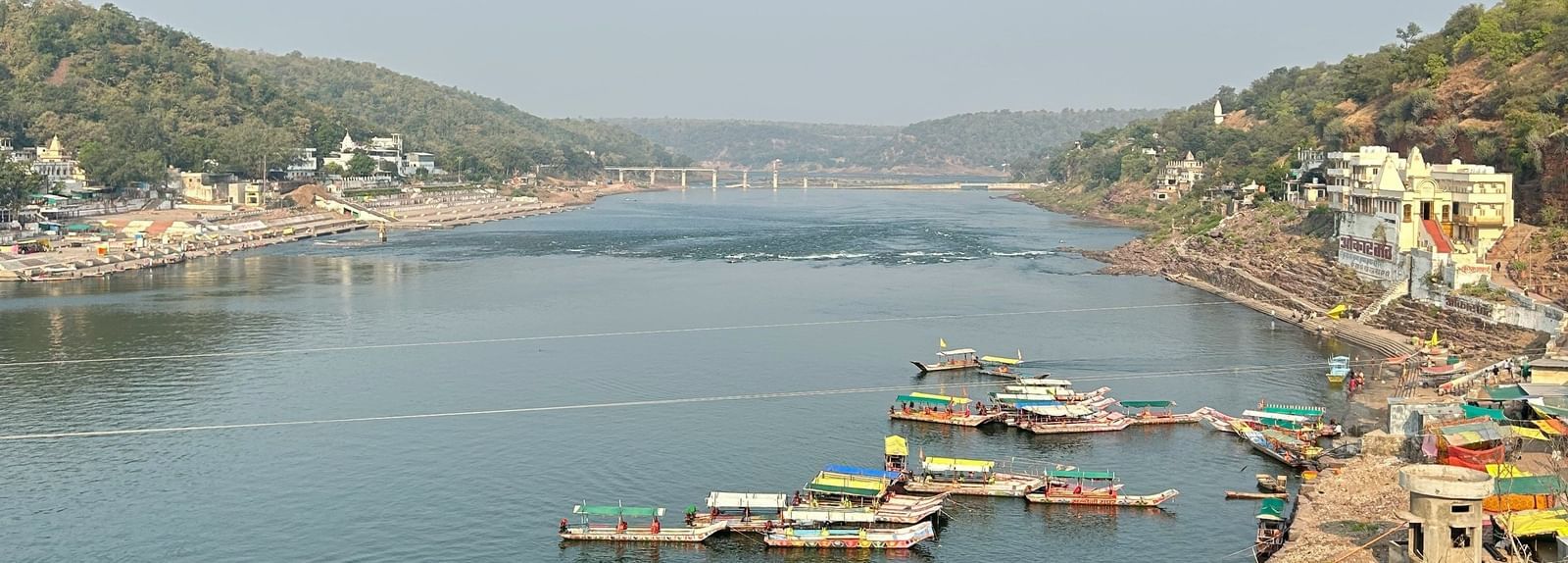 Boats lined along the riverbank with hills in the background.