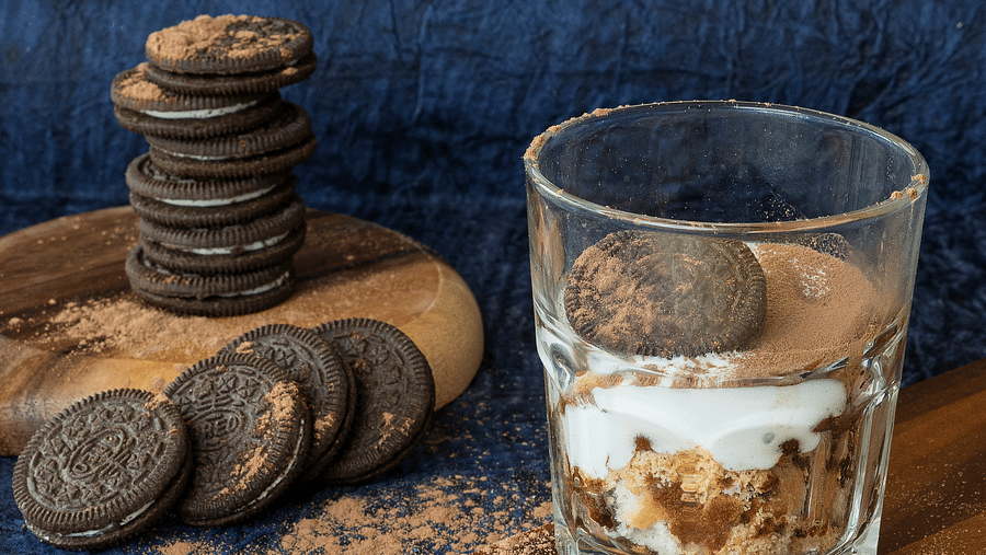 An image featuring a glass of caramel chocolate alongside cream biscuits, with a stack of several biscuits placed on top of each other.
