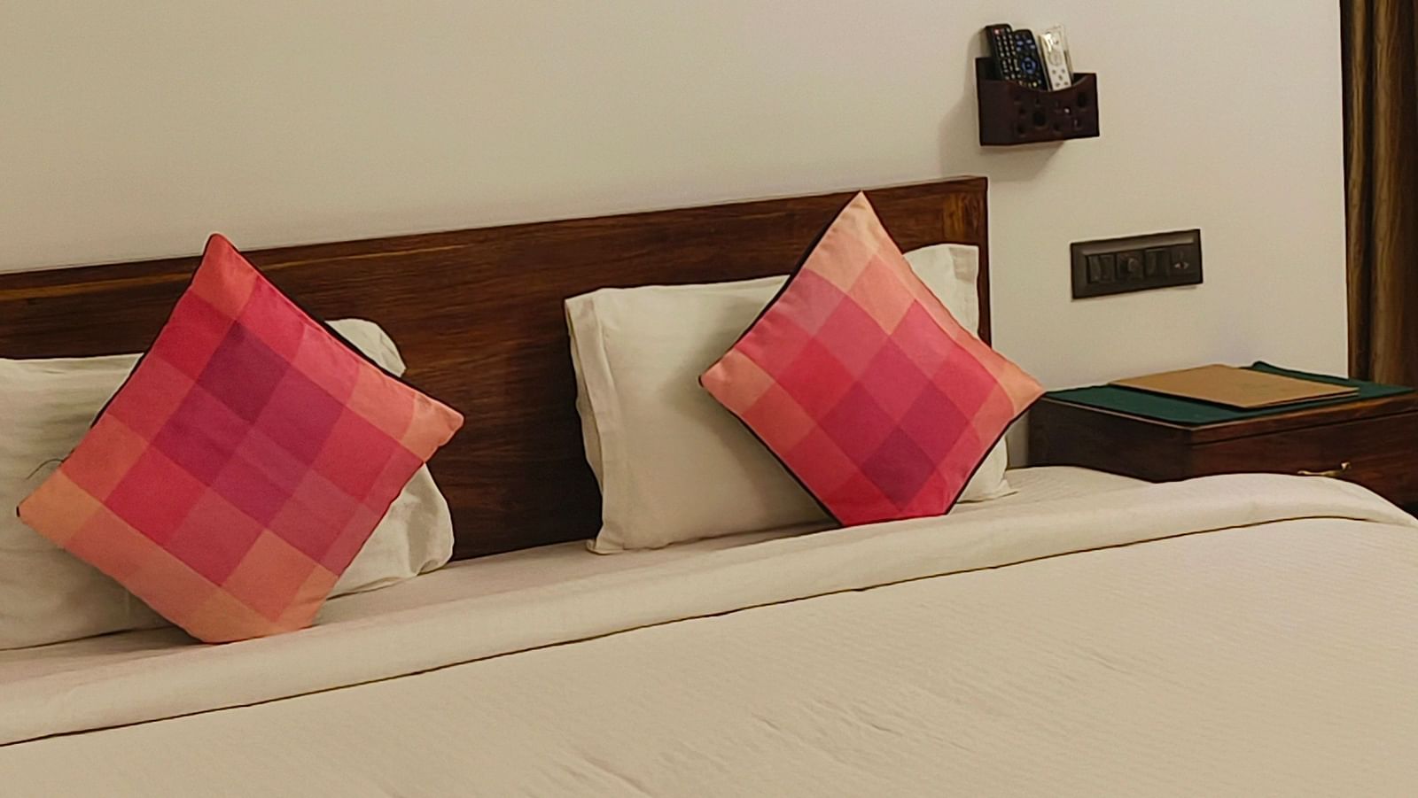 Front view of a double bed with two pink pillows kept on it and hexagonal frames hanging on the wall in 101 non-ac room at Ananda Holiday Home, Wayanad 1
