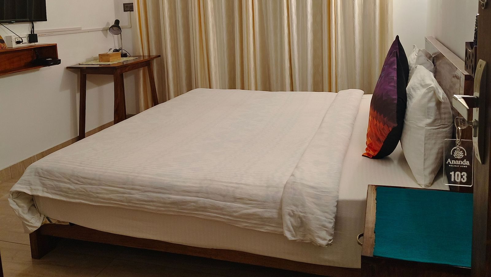 Side view of the double bed in 103 room along with cream coloured curtains on the window at Ananda Holiday Home, Wayanad 8