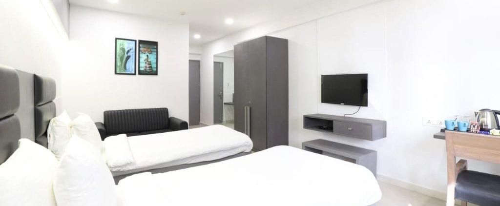 A wide-angle shot of the Premium Twin Room featuring 2 single beds along with a wardrobe and a wall-mounted television in front of it at Pravasa Stay, Ahmedabad (Alba Premier).