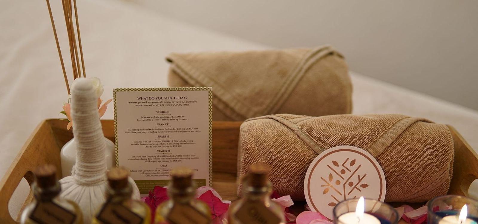 A pair of candles placed alongside some essential oils and towels on a tray in a spa
