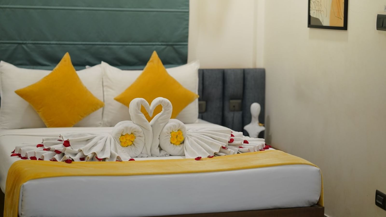 A room with a neatly made double bed adorned with yellow and towels shaped into swans, scattered with rose petals for a welcoming touch at Hotel Kyzen Smartstays – Smart, Reliable, Kyzen