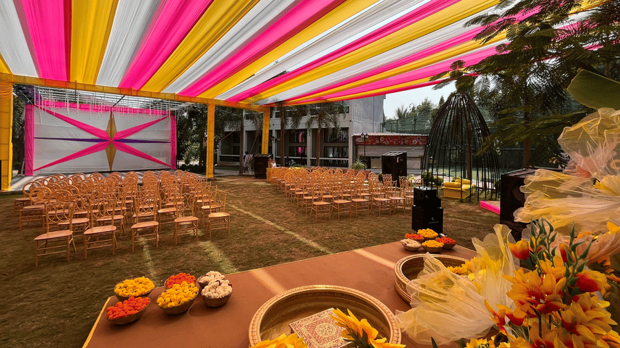 Outdoor event setup with pink and yellow ceiling drapes and rows of gold chairs for guests - DAN Resorts & Weddings, Palghar