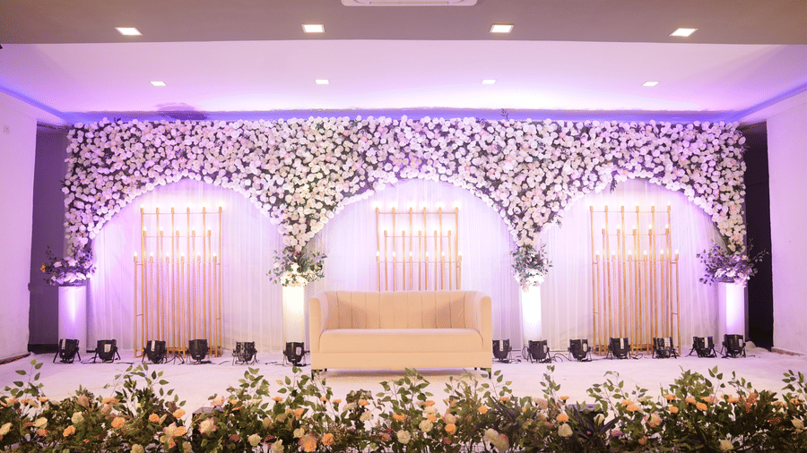 Beautifully decorated indoor wedding stage featuring floral arches and a plush cream sofa - DAN Resorts & Weddings, Palghar