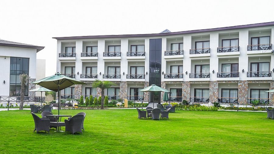 Resort lawn with seating areas under umbrellas, surrounded by well-maintained greenery and modern guest rooms - Shervani Pebbles & Pines, Corbett