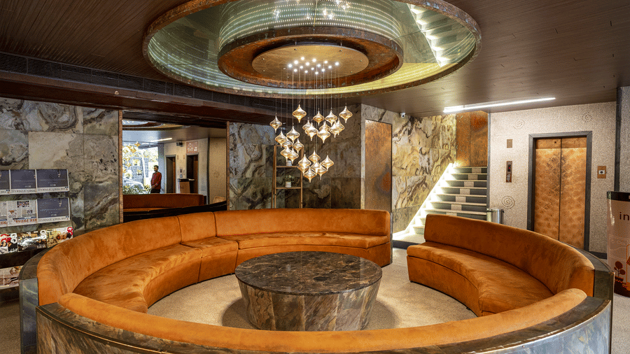 Interior of a lobby with circular wooden seating, a modern chandelier, and polished stone surroundings at Infiniti Hotel, Indore.