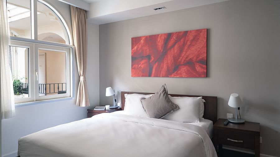 A bedroom with a large bed, a nightstand, and a piece of art on the wall | Two-bedroom Suite | Central Mansions, Phnom Penh