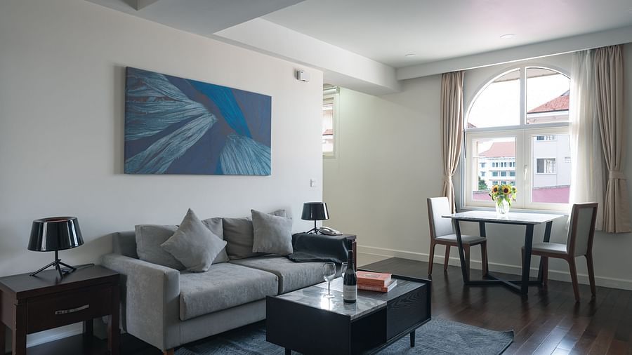 A living room with a grey sofa, a coffee table, and a dining table | One-bedroom Suite | Central Mansions, Phnom Penh