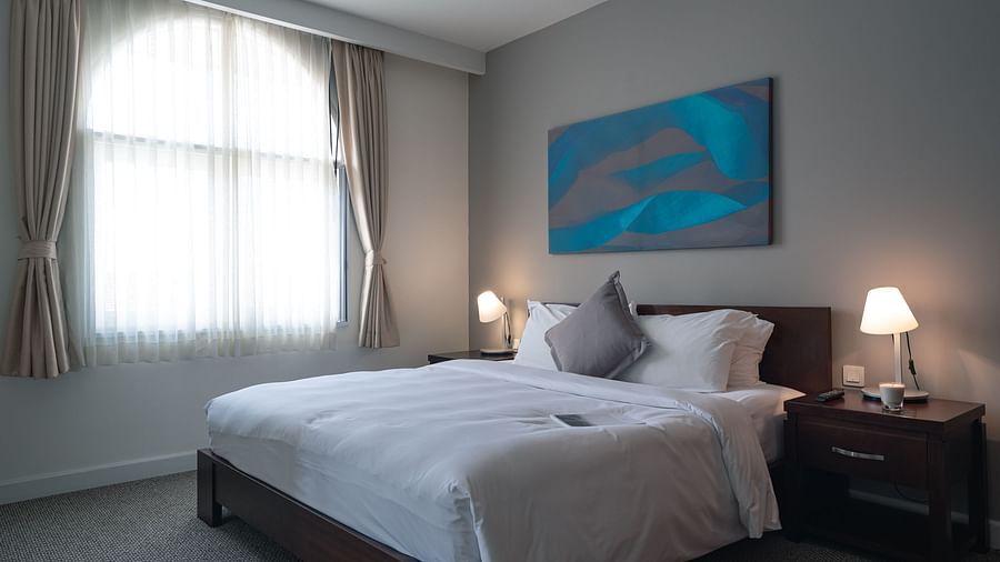 A well-lit bedroom with a large bed, a nightstand, and a modern painting above the headboard | One-bedroom Suite | Central Mansions, Phnom Penh
