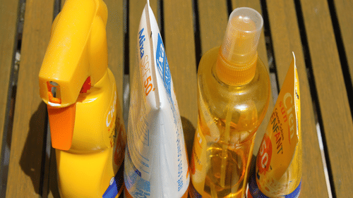 A close up of four different types of sunscreen on different types of bottles kept on a bench.