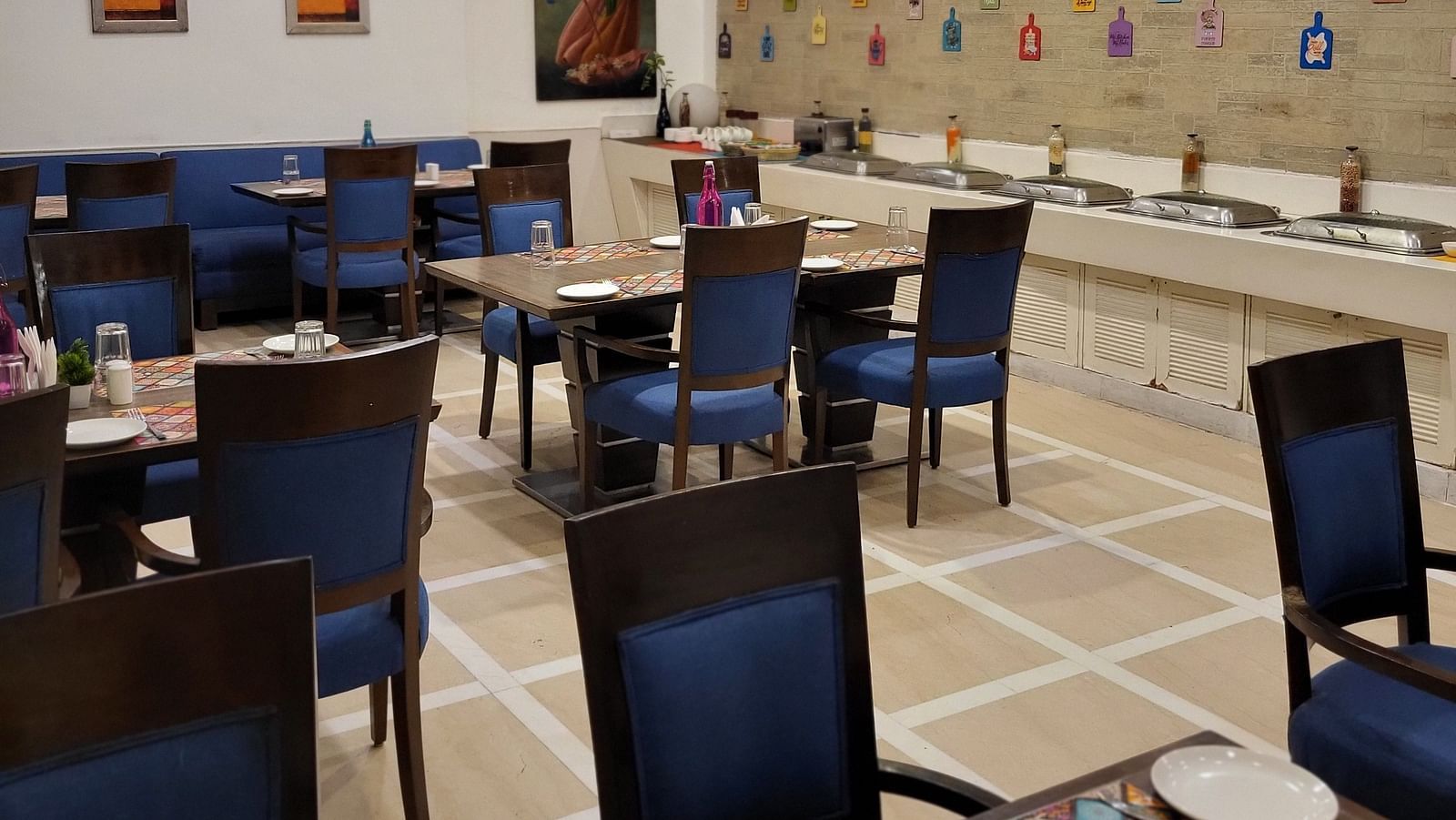 An image of a restaurant featuring multiple sets of chairs and tables where plates, cutlery and napkins are placed at Inde Hotel Signature Tower Gurgaon