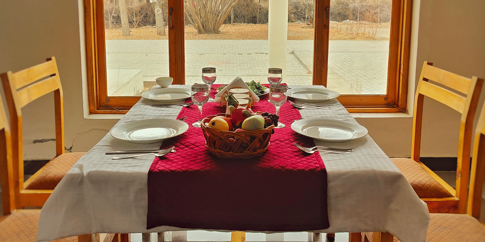 A wooden dining table for four set neatly in front of a large window with a scenic view at Indus Serenity Retreat.