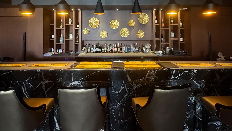 A dimly lit bar with a dark, textured wall and a row of bottles illuminated from behind, highlighting the bar's moody atmosphere.