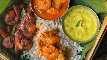 A wooden box lined with a banana leaf containing rice topped with prawn curry, served with fried prawns and tempered yoghurt.