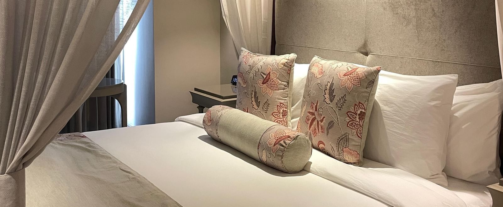 A side view of the four-poster bed in a Premium King Room at The Evren, Vagator. The bed is dressed with a bed runner and decorative pillows, and the white curtains are tied back, letting in natural light.