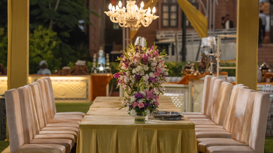 A dining table with a gold tablecloth and chairs, decorated with hanging gold tinsel and a chandelier at Garh Govind.