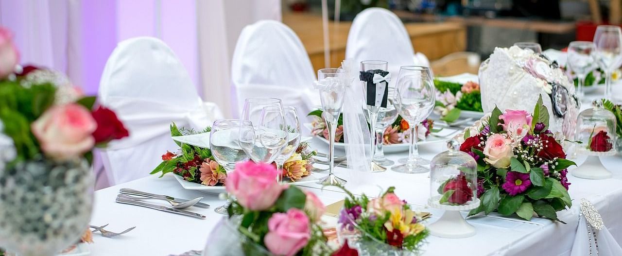 Close up shot of a dining table decorated with several flower bouquets along with shiny glassware.  