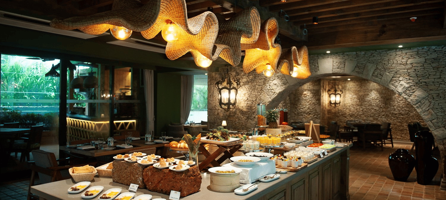 A lavish breakfast buffet spread at the Mila Restaurant at The Evren, Vagator, featuring a variety of dishes on display under the woven light fixtures.