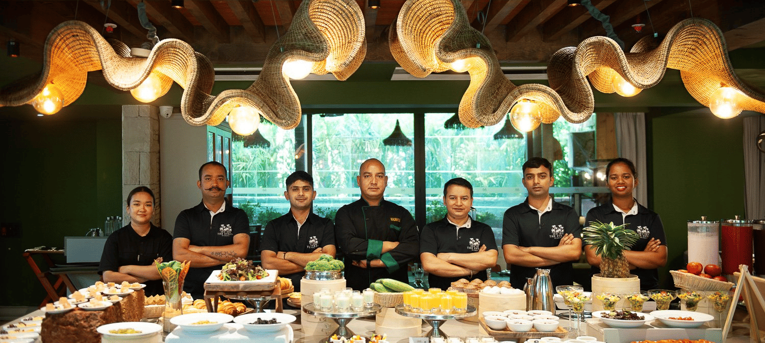 A proud team of chefs dressed in black chef coats at the Mila Restaurant at The Evren, Vagator, standing behind a beautifully presented buffet spread.