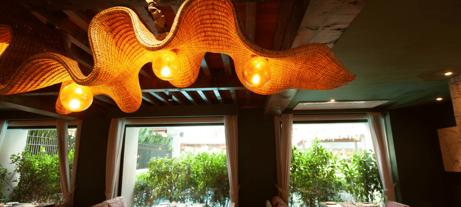 A wide-angle shot of the interior of the Mila Restaurant at The Evren, Vagator, highlighting the unique, woven light fixtures hanging from the wooden ceiling.