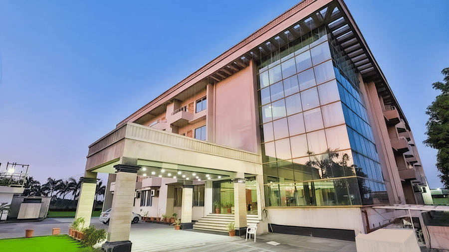 Facade of Biznotel by Pride, Bharuch with glass exterior, entrance steps, and driveway surrounded by greenery.