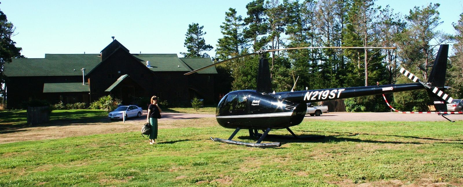 A woman dressed in black walking from a barn type building towards a helicopter ready to take off - Brewery Gulch Inn & Spa