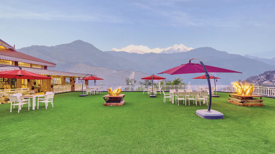 Open-air event lawn with dining tables, red parasols and lit fire pits, overlooking the snow-capped Kanchenjunga range at MAYFAIR Himalayan Spa Resort, Kalimpong.