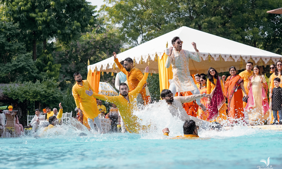 Joyful haldi ceremony with guests celebrating in a poolside setting.