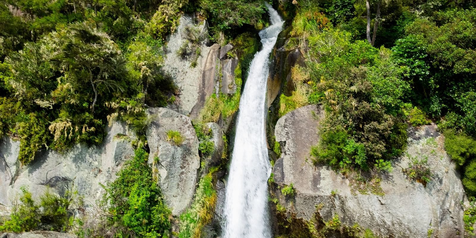 an overview of a waterfall getting collected into a waterbody with blue sky in the background.
