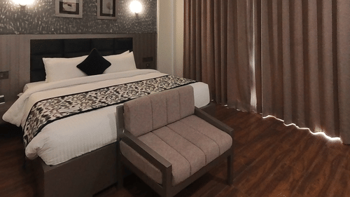A room at Grand Continent, Anjuna featuring a large bed, a small sofa, dark curtains, and patterned walls with decorative lights.