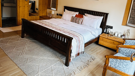 The well-lit Standard Room at Megha Resorts & Villas, featuring a large bed with linens, wooden walls and ceiling, a ceiling fan, and a wall art.