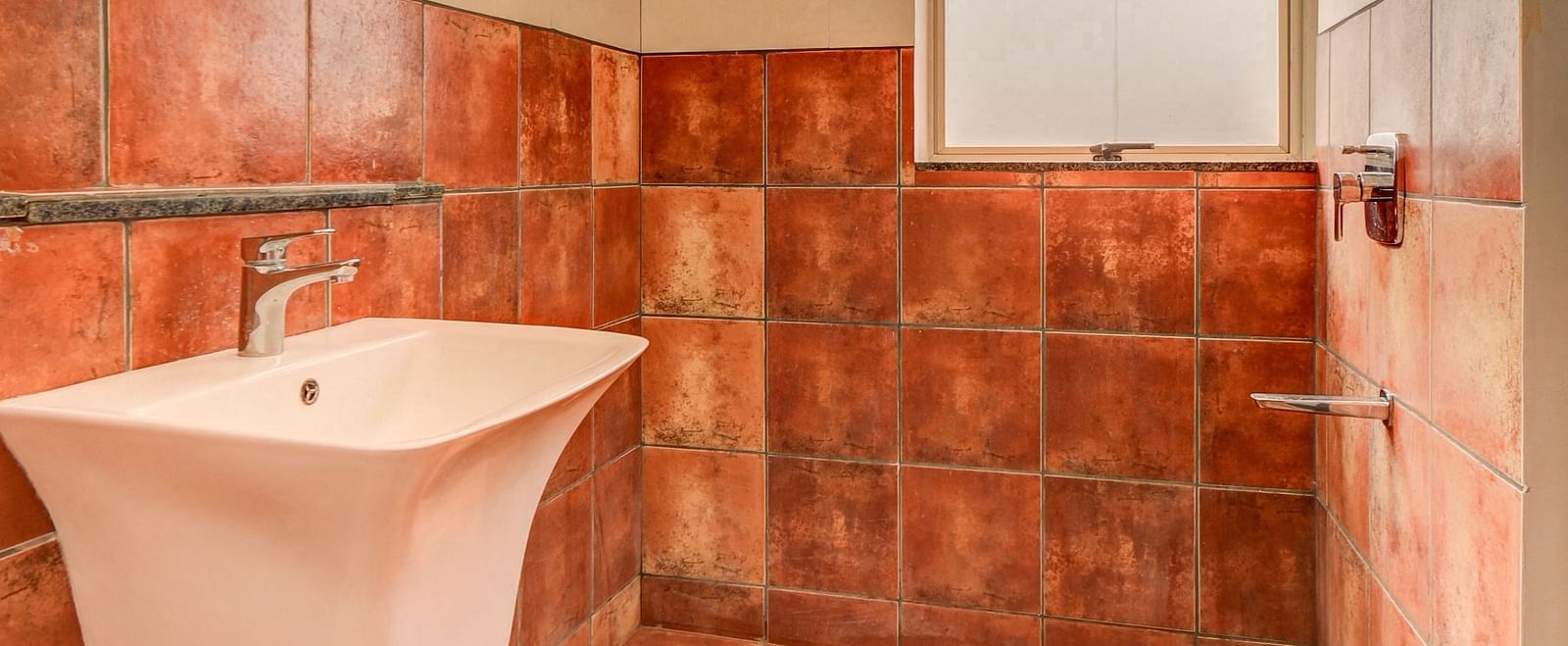 A spacious washroom at Harigovinda's JNStay, with a washbasin to the side and a shower head at the furthest end