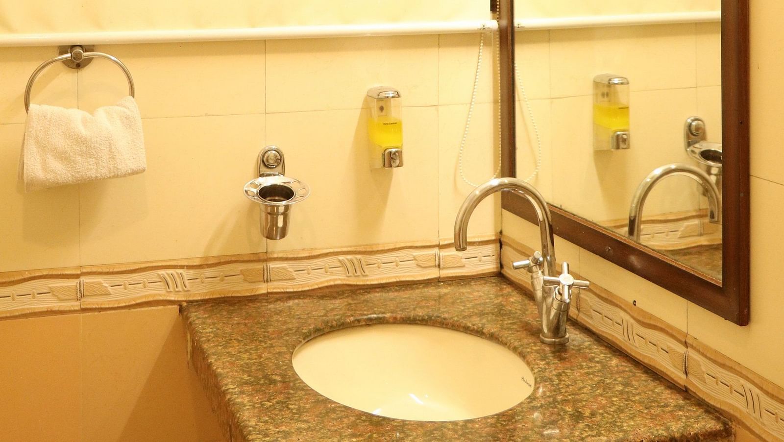A bathroom with a round sink on a granite countertop, a framed mirror, and a towel ring, illuminated by a light fixture above. - Hotel Diamond Plaza, Chandigarh.