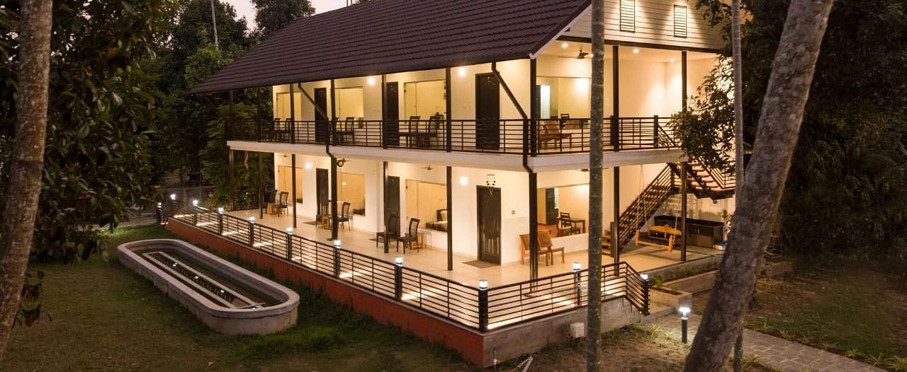 An exterior view of a well-lit, multi-story building at dusk, the Lhasa Ayurveda & Wellness Resort, with surrounding greenery.