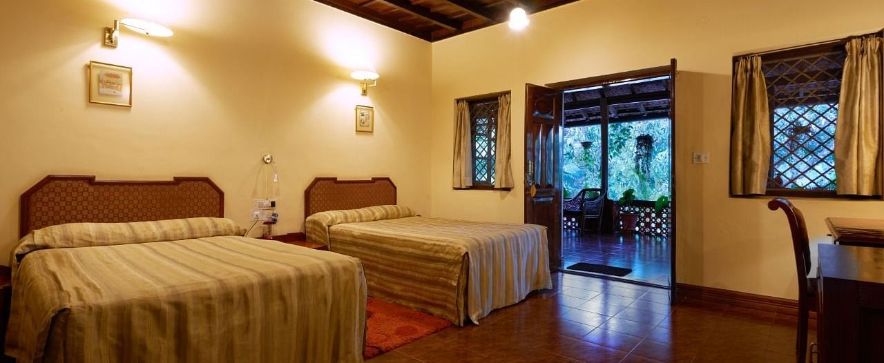 Spacious room with twin beds, wooden ceiling beams, and windows showing greenery - BluSalzz Collection - Tranquil Resort, Wayanad
