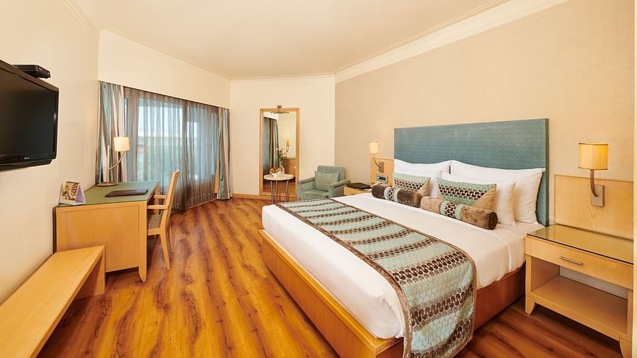 Image of a room at Pride Hotel Nagpur featuring a plush bed with cushioned wooden headboard with wooden nightstands on both sides facing the TV mounted on the wall
