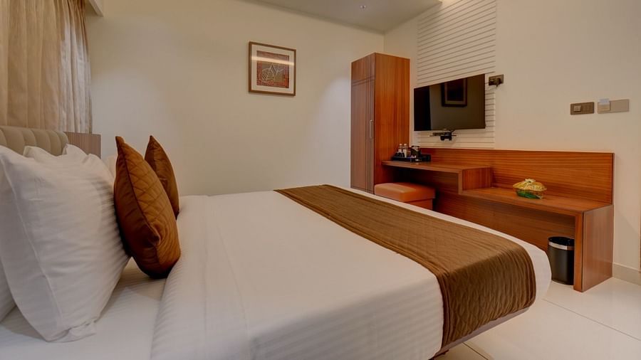 An image of a room featuring a bed with a wooden table in front, and a television mounted above it at Hari Govindas, Siddappa Square.