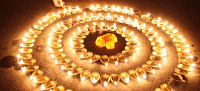 A person in a red outfit kneels to arrange lit candles in a large circular pattern on the ground.