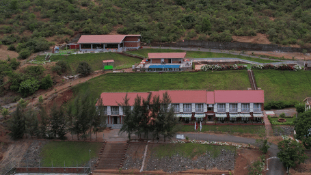 An aerial view of a resort with a large lawn and a swimming pool, surrounded by green hills - Lords Hotels & Resorts