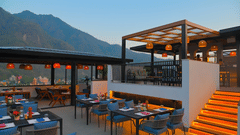 Rooftop dining area at The Terrace, Aloha on the Ganges, Rishikesh, featuring outdoor seating, illuminated staircase, and mountain views at dusk.