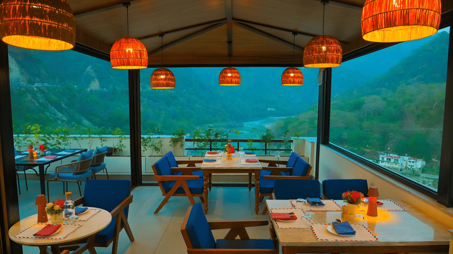 Window side dining area at The Terrace, Aloha on the Ganges, Rishikesh, overlooking the surrounding mountains through floor to ceiling glass panels.