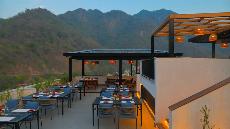Open air dining space at The Terrace, Aloha on the Ganges, Rishikesh, with neatly arranged tables, rooftop seating, and scenic mountain views.