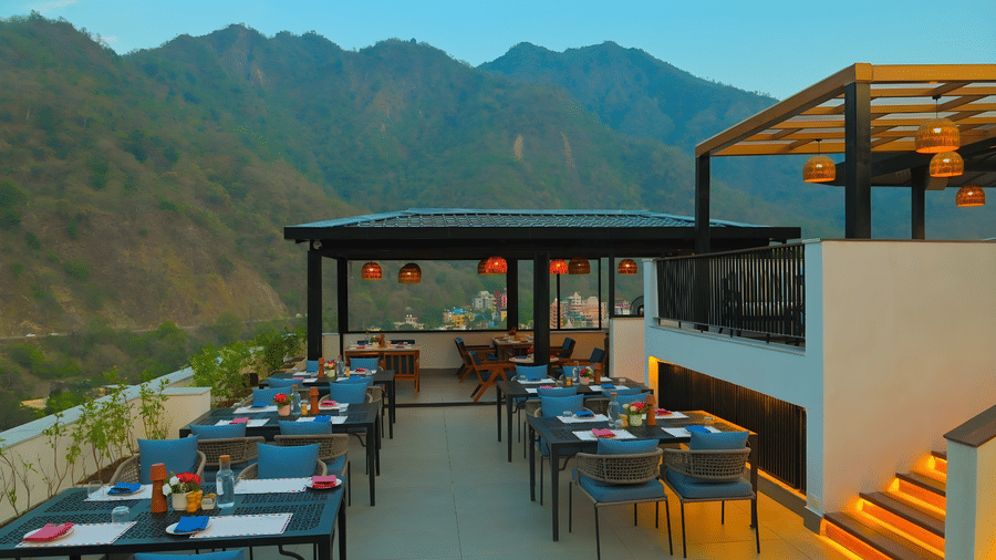 Spacious rooftop restaurant at The Terrace, Aloha on the Ganges, Rishikesh, featuring outdoor tables, ambient lighting, and panoramic mountain views.