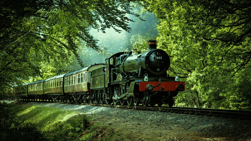 A toy train moving along on the tracks with nature surrounding it