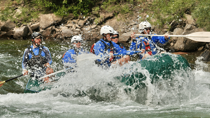 Group of rafters navigating rapids, water splashing around them.