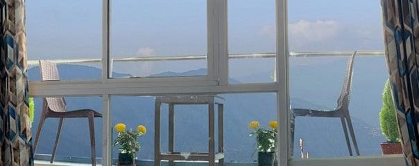 Balcony with two chairs, one table with small plants placed near the chairs and a big glass window at A room with double bed, Framed art work on the wall, TV, Wardrobe, Dustbin, Table and desk with two water bottles on the top at Central Heritage Resort an